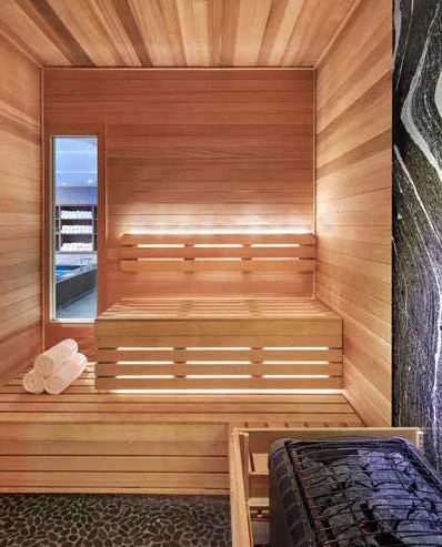 Serenity: Under-bench and backrest LED lighting, a marble slab behind the heater, and a pebbled floor define this commercial sauna.